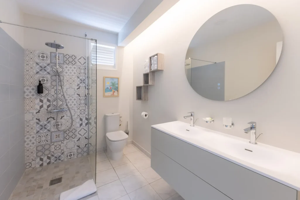 Salle de douche partagee Villa Bel Embrun Salle de bain moderne avec douche, lavabo double et miroir rond. Décor épuré et lumineux.