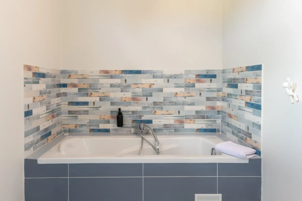 Salle de bain Villa Bel Embrun Baignoire moderne avec carrelage bleu et beige sur les murs. Serviette posée à côté.