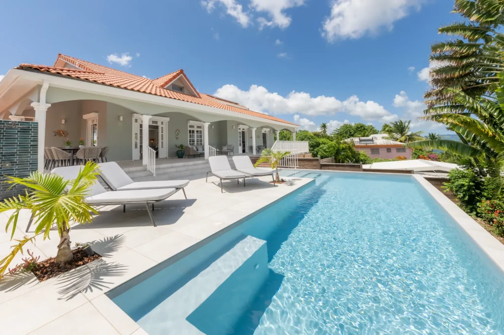 Villa Bel Embrun Villa moderne avec piscine, chaises longues et jardin tropical sous un ciel bleu.