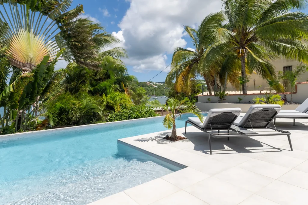 Piscine Piscine avec chaises longues, entourée de palmiers et d'une vue sur l'eau.