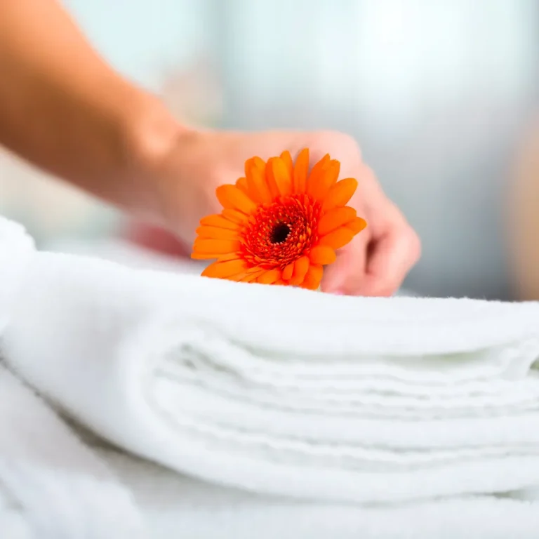 Personnel de menage Main dans une serviette pliée, tenant une fleur orange.