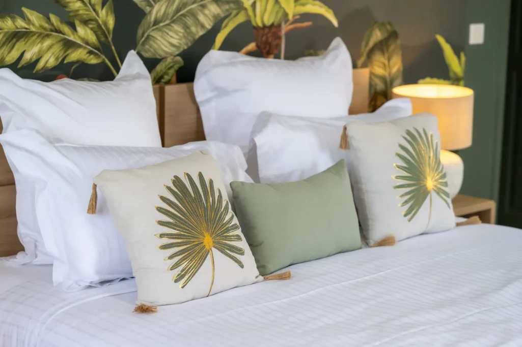 Chambre Tropicale Couchage avec coussins décoratifs sur un lit, murs avec motifs de plantes.